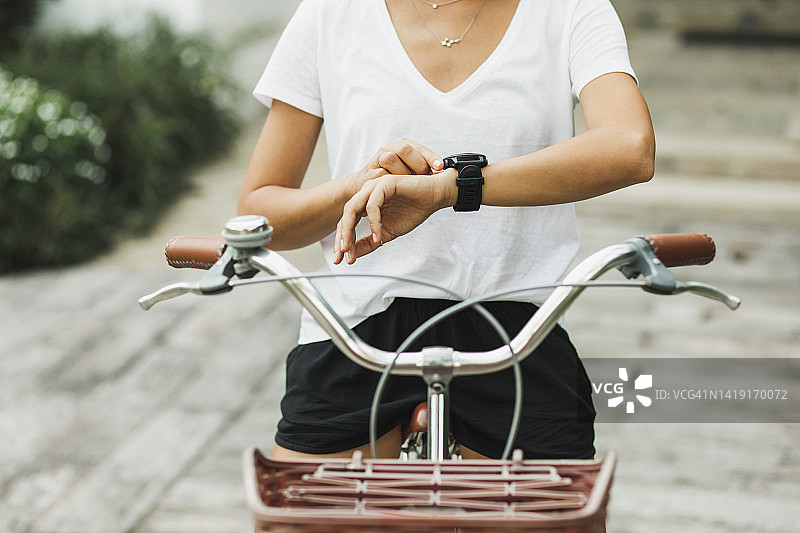 女子按下智能手表上的按钮以启动骑自行车应用程序。运动中的小工具。无法辨认的人图片素材