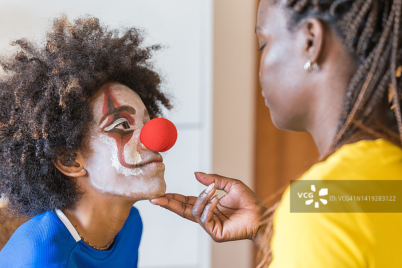 特写：母亲看着化完妆、戴上小丑鼻子的儿子微笑图片素材