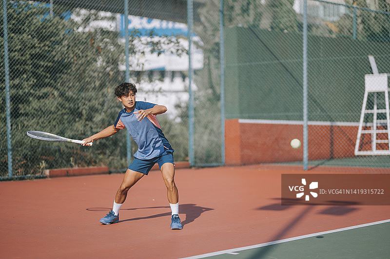 在硬地球场打网球的年轻亚洲男子网球运动员图片素材