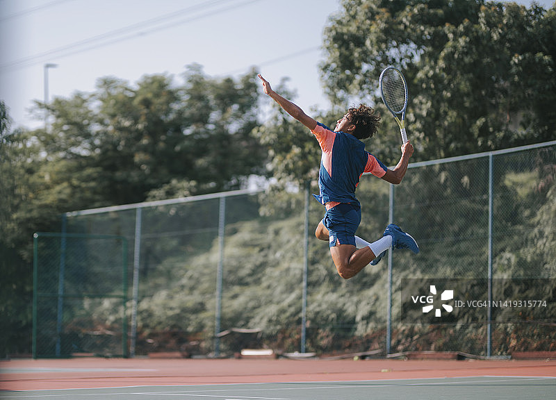 在硬地球场上跳跃发球的亚洲网球男运动员图片素材
