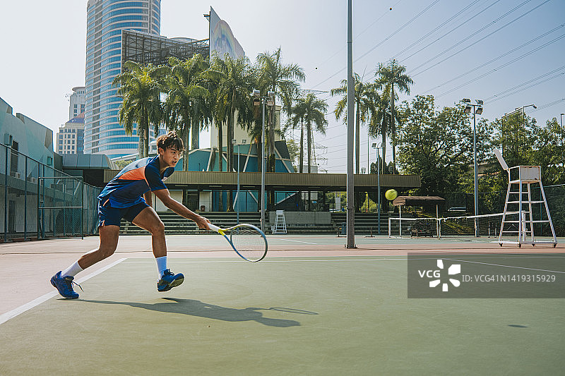在硬地球场上救球的亚洲网球运动员图片素材