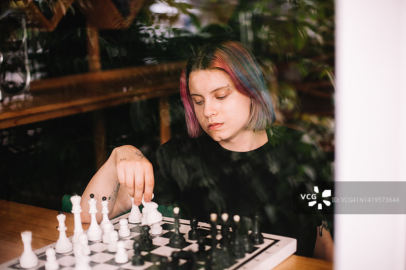 年轻女子在咖啡馆靠窗独自下棋图片素材