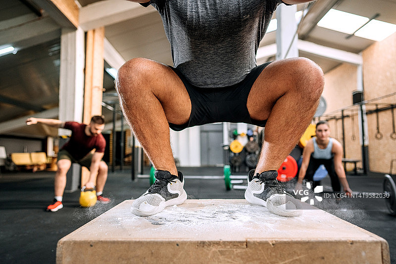 在健身房充满活力地跳箱子的健壮男人图片素材