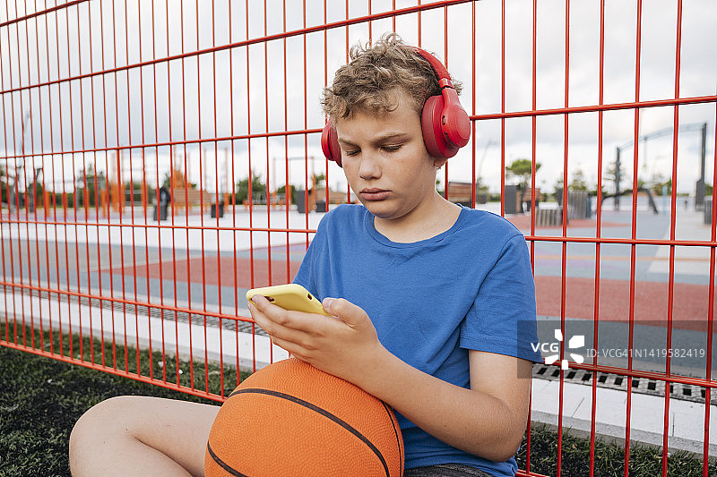 在操场上带着篮球和耳机男孩的肖像图片素材