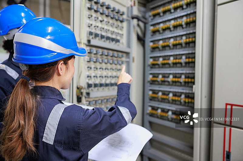 两位亚洲工程师在变电站电气控制室使用平板电脑检查配电开关设备状态图片素材