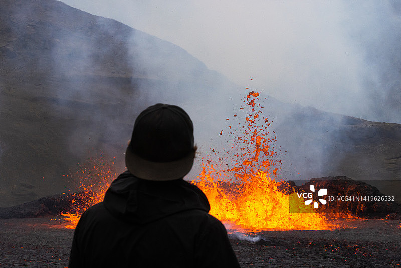 在冰岛，一位游客站在正在喷发的火山附近图片素材