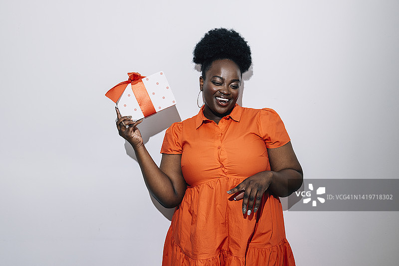 一位快乐的混血女人拿着一个橙色和白色的礼物盒站着（白色背景隔离）图片素材