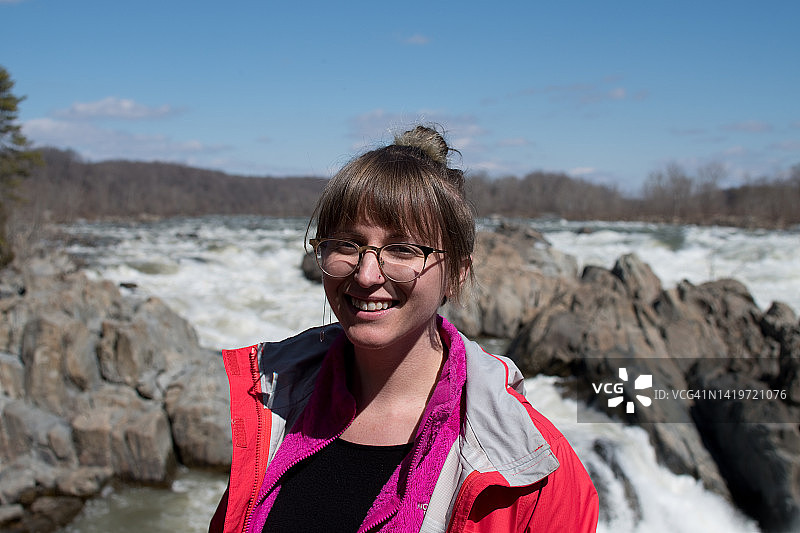 戴眼镜的女徒步旅行者在瀑布前图片素材