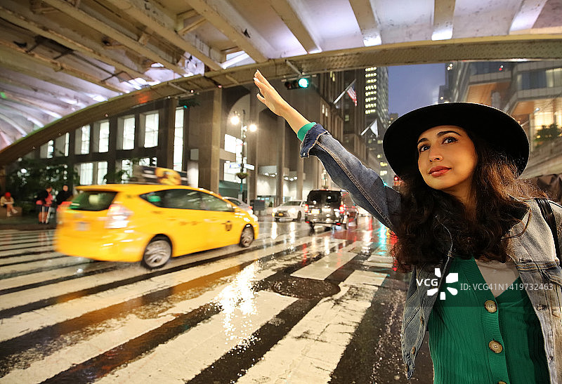 美丽的女人在纽约市波斯广场、中央车站外第42街的暴风雨之夜招手拦出租车图片素材