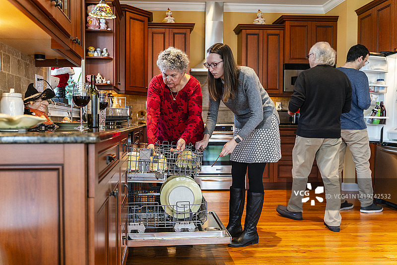 节假日期间成年子女探望年迈的父母，在厨房帮忙将脏盘子放入洗碗机图片素材