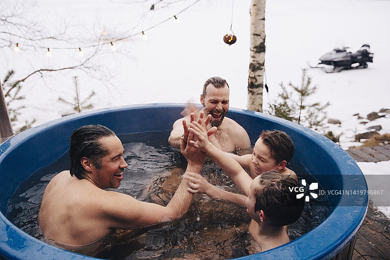 在热水浴缸里互相击掌的快乐中年男人和男孩图片素材