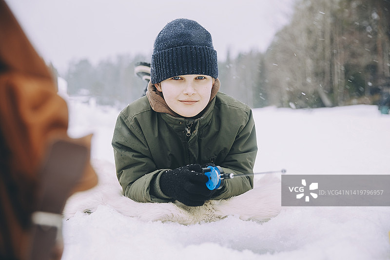 针织衫微笑男孩躺在雪地上的肖像照图片素材