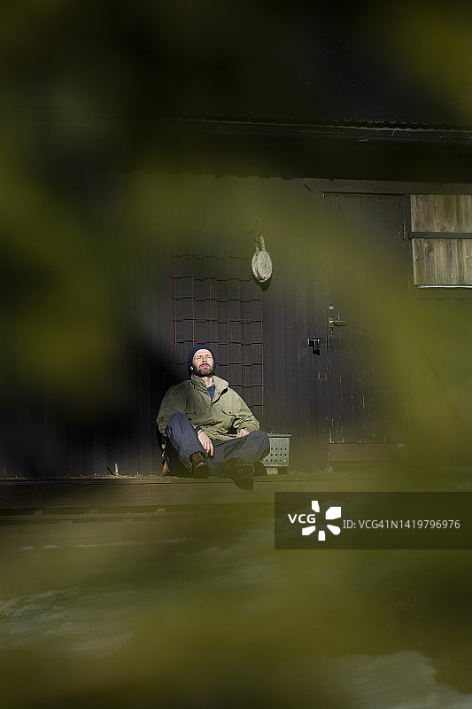 在晴朗的日子里坐在门廊上闭着眼睛的中年男人全身照图片素材