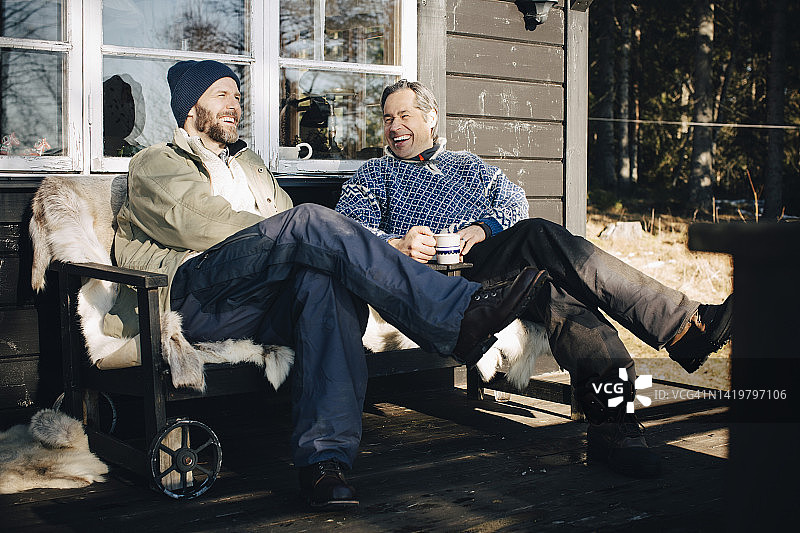 笑容满面的中年男人在冬季的门廊一起喝咖啡聊天图片素材