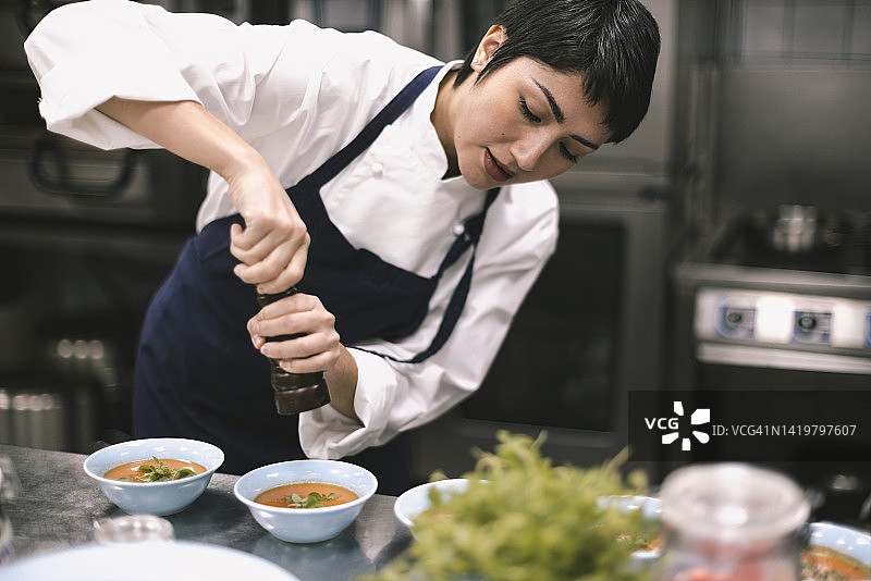 餐厅厨房里，女厨师在料理台上给汤加胡椒粉图片素材