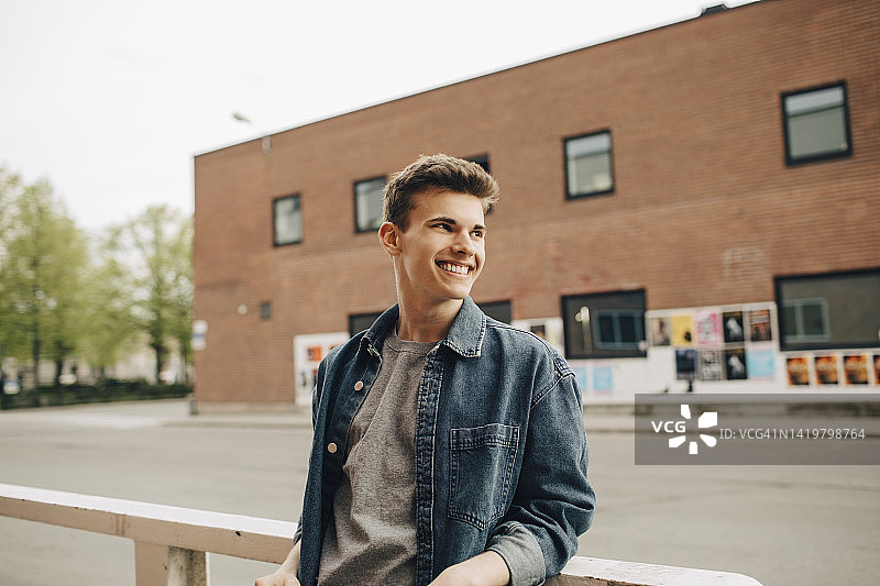 微笑的年轻人靠在栏杆上，看向远方图片素材