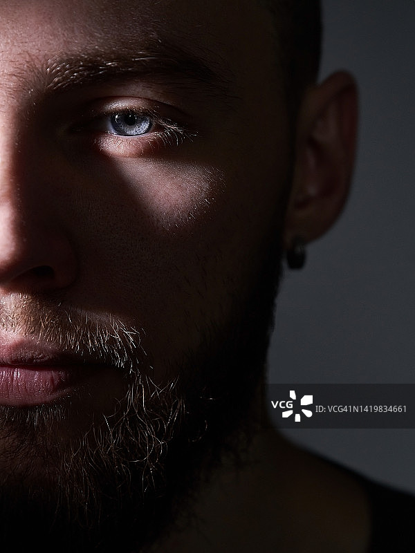 留着胡子、小胡子、蓝眼睛的粗犷男人的半张脸，灰色孤立背景。严肃的中年男子戴着耳环的特写。图片素材
