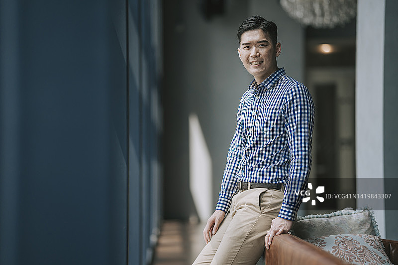 休闲商务装的亚洲男人靠在沙发上对着镜头微笑图片素材