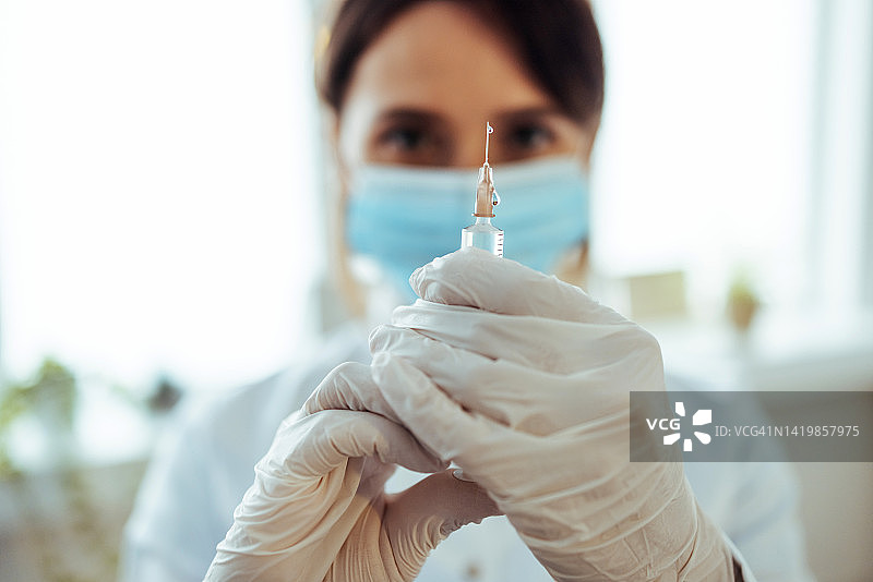 年轻医生拿着装有新冠疫苗的注射器，准备进行新冠疫苗接种图片素材