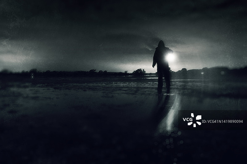 一个神秘的蒙面人拿着一盏灯，在乡村一片被洪水淹没的田野中度过一个幽灵般的冬夜，并进行了纹理编辑图片素材