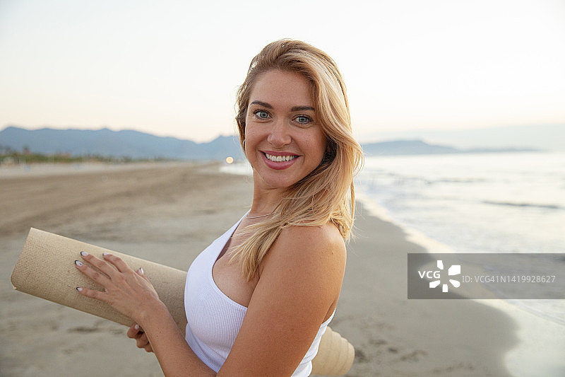 在海滩上手持瑜伽垫看向镜头的女人图片素材