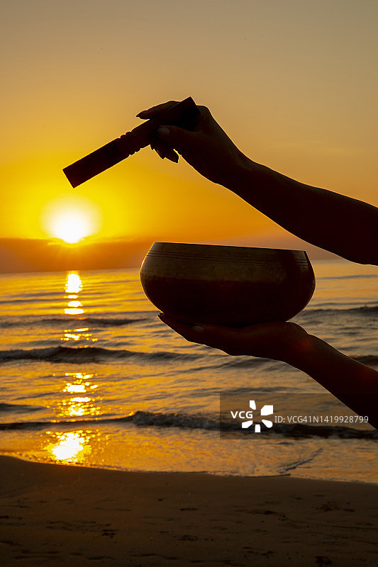 在海滩日出时用颂钵冥想的女人图片素材