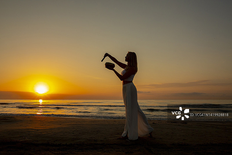 在海滩日出时用颂钵冥想的女人图片素材