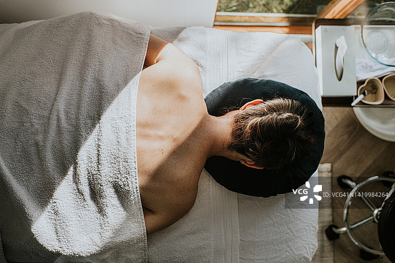 一名女子脸朝下躺在按摩台上，身上盖着毛巾，露出裸露的肩膀和上背部图片素材