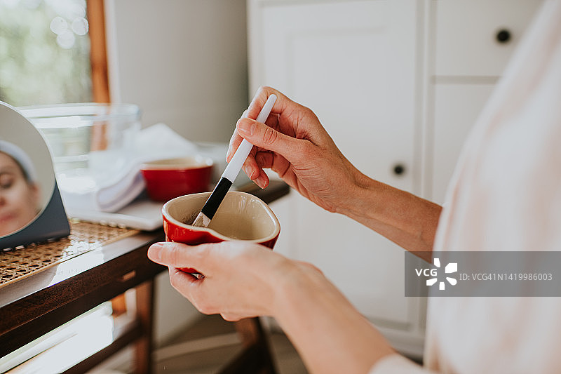 穿着浴袍的女人用化妆刷在碗里搅拌面膜的特写图片素材