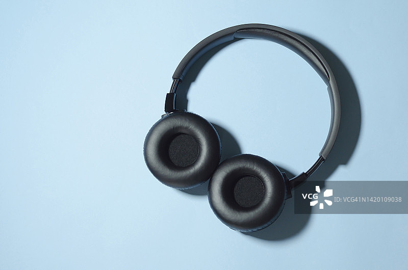 蓝色背景上的黑色无线耳机：现代科技概念图片素材