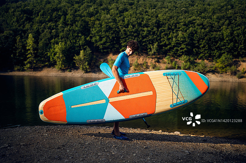 携带立式桨板在湖边行走的白人男子图片素材