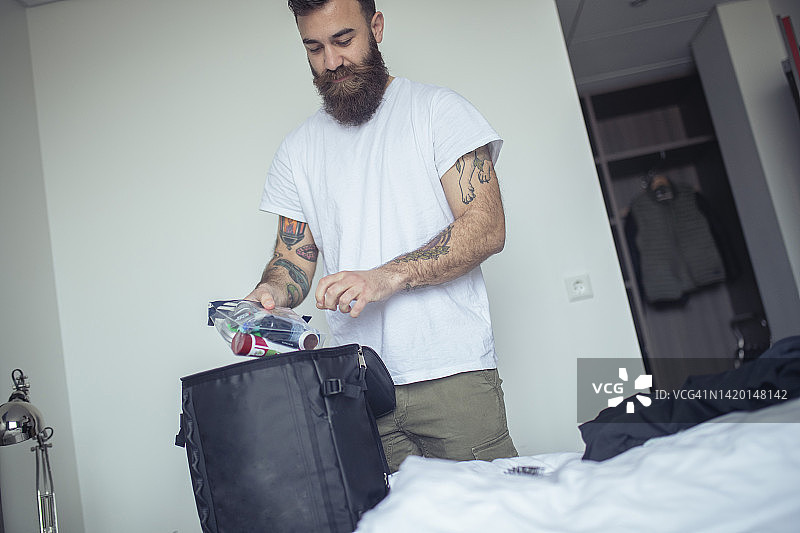 一个时髦的男人把东西装进包里，准备离开酒店房间。图片素材