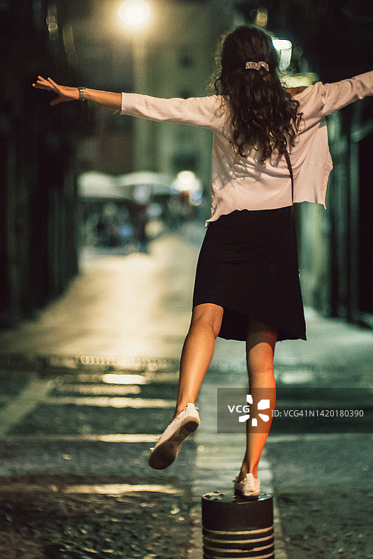 夜晚站在街上单腿抬起手臂的年轻女子背影图片素材