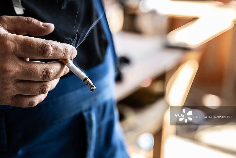 一名男工手中燃烧的香烟上的长长烟灰。图片素材