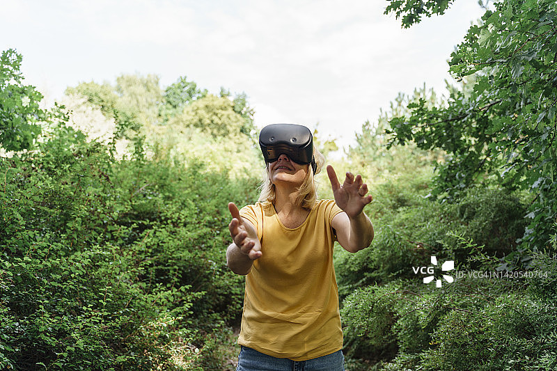 站在植物中的中年妇女用虚拟现实模拟器做手势图片素材