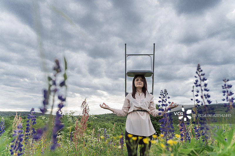 自由职业者在草地上冥想，头顶椅子图片素材