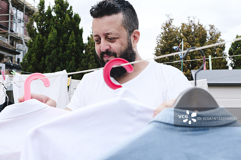 微笑的男人在后院的晾衣绳上晾衣服图片素材