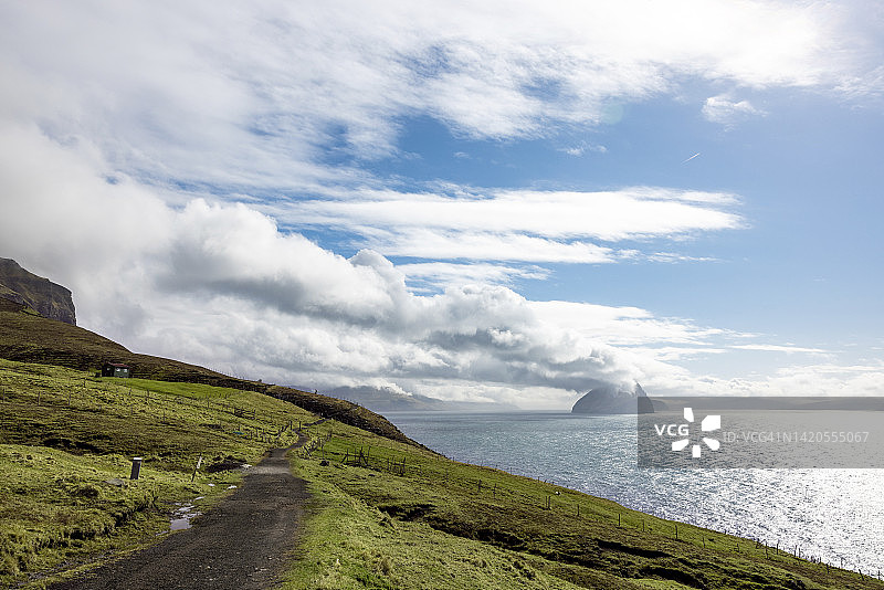法罗群岛瓦加尔岛：海岸土路上的云朵，背景是岛屿图片素材