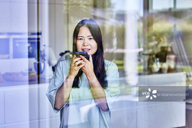 透过玻璃看中年妇女用手机发送语音邮件图片素材