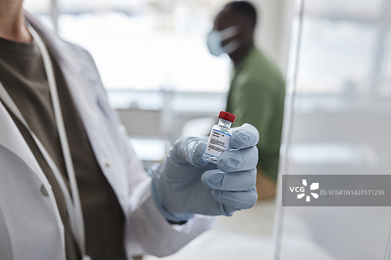 医生戴着手套拿着COVID-19疫苗图片素材