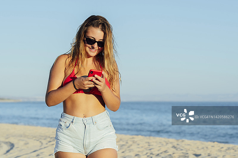 在海滩上边走边用智能手机打字的女人图片素材
