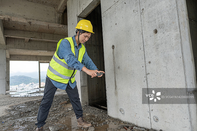 在建筑工地上用手机拍照的亚裔女工图片素材