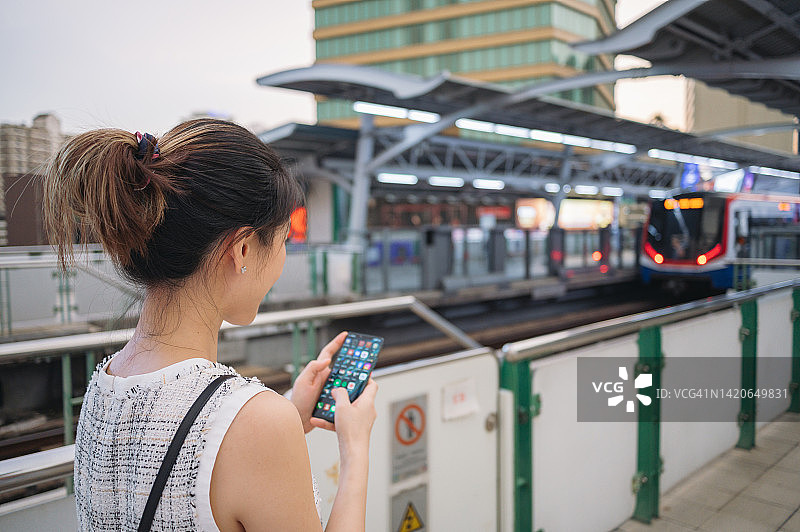 在泰国曼谷，中年亚洲女商人使用手机通过社交网络在轻轨上享受周五，等待火车图片素材