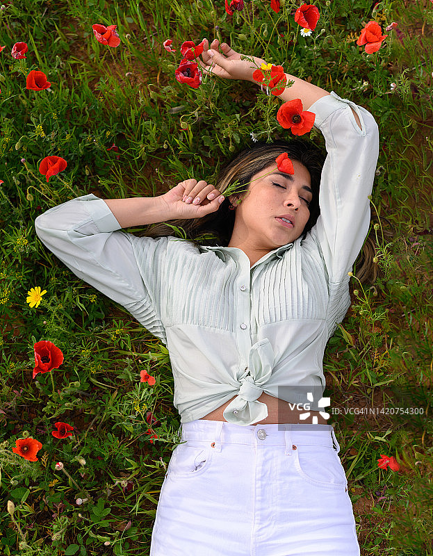 在盛开的草地上闭目放松的年轻西班牙裔女士图片素材