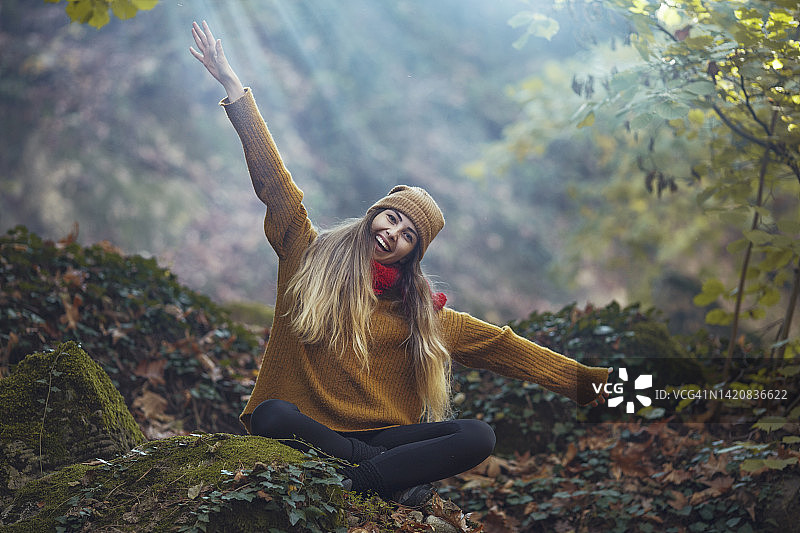 微笑的年轻女子在森林里呼吸新鲜空气，举起双臂图片素材
