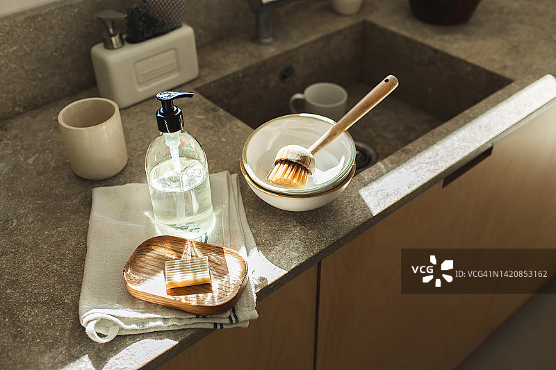 石制厨房台面上水槽旁的木制皂托、清洁刷、毛巾和有机清洁剂图片素材