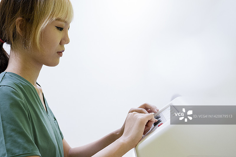 操作骨密度扫描仪的亚裔美国女技术员侧面半身照图片素材