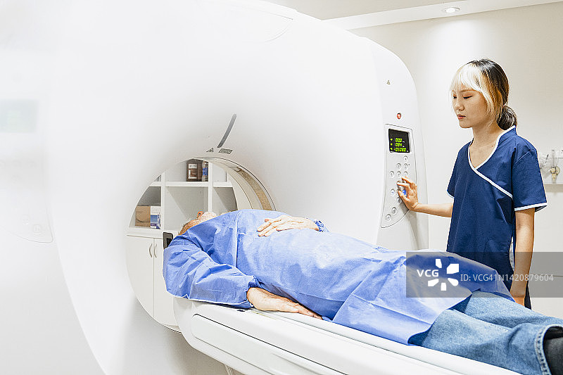 年轻的亚裔美国女技术员操作核磁共振扫描仪，男性病人正在接受测试的中景镜头图片素材
