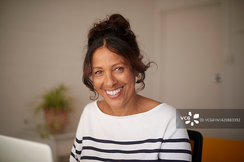 中年妇女在家中客厅使用笔记本电脑进行博客创作，撰写书籍或构思创意。微笑的自由职业者、作家或代笔作家通过互联网技术获取电子书灵感图片素材