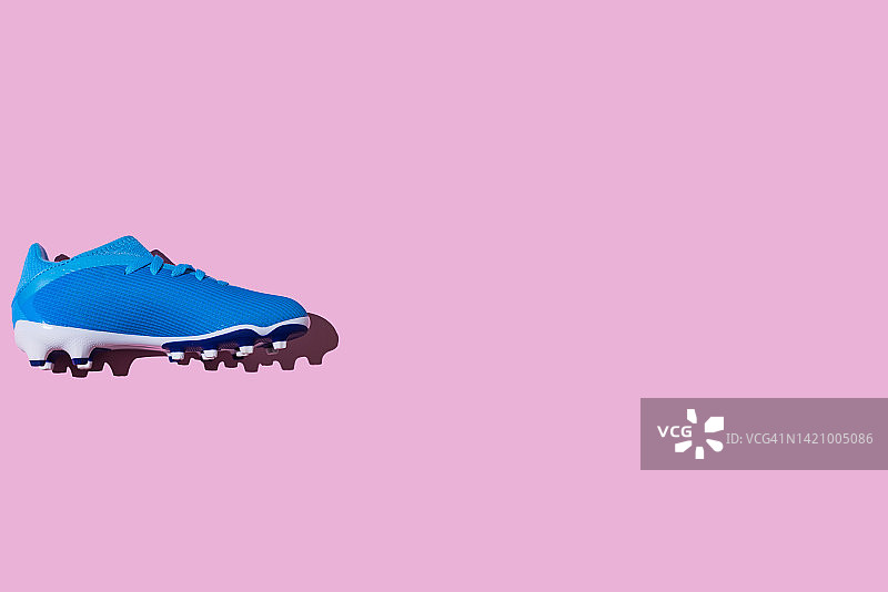 粉色背景上的蓝色足球鞋，足球、世界杯、运动、卡塔尔、运动鞋和女子足球概念图片素材
